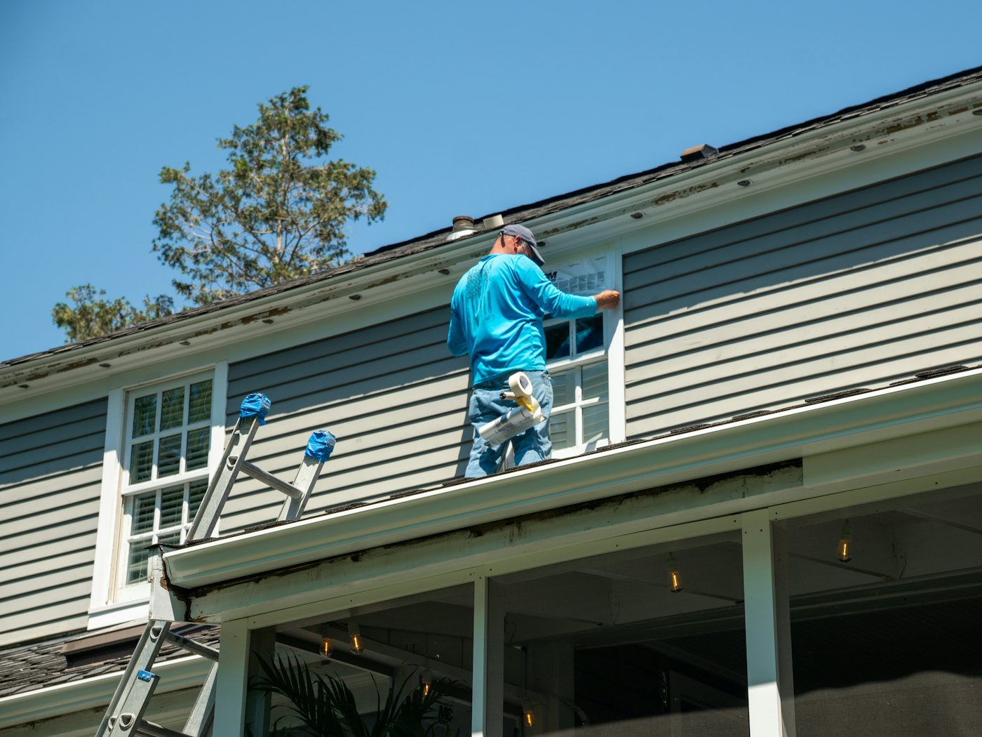 Painter in a company shirt masking a window on lap siding before painting